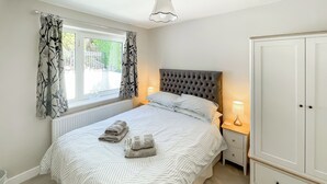 A bedroom with a bed, two bedside lamps, a wardrobe, and a window with curtains. - A beautiful bungalow, quiet location with beautiful views. (Keswick)