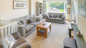 A spacious living room with a grey sofa, a wooden coffee table, and a bookshelf. - A beautiful bungalow, quiet location with beautiful views. (Keswick)