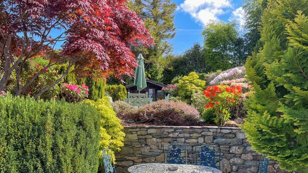 A garden patio with a stone wall, a round table, and blue metal chairs. - A beautiful bungalow, quiet location with beautiful views. (Keswick)