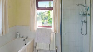 A bathroom with a bathtub, a shower, a window with curtains, and a view of greenery outside. - 2 bedroom accommodation in Cinderford (Cinderford)