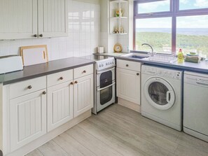 Een keuken met witte kastjes, een spoelbak, een fornuis, een oven en een wasmachine.