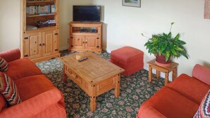 A living room with a sofa set, a coffee table, a television on a wooden stand, a bookshelf, and a potted plant. - 2 bedroom accommodation in Cinderford (Cinderford)