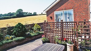 A brick house with a wooden deck, a fenced garden, and a field in the background. - 1 bedroom accommodation in Apse Heath, near Shanklin (Apse Heath, near Shanklin)