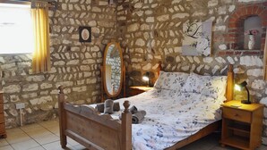 Ein Schlafzimmer mit Steinwänden, einem hölzernen Bett, einem Nachttisch mit Lampe und einem Spiegel an der Wand.