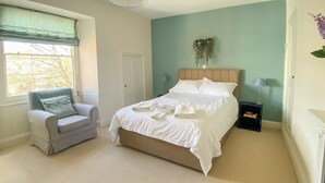 Une chambre bien rangée, avec un lit, une chaise, une table de chevet et une fenêtre donnant sur des arbres.