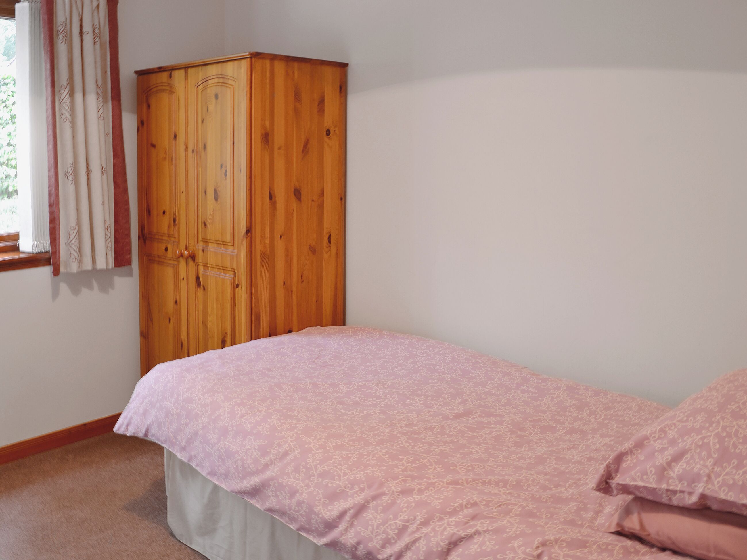 Ein Schlafzimmer mit einem Einzelbett, einem Holzschrank und einem Fenster mit Vorhängen.