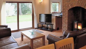 Ein Wohnzimmer mit Kamin, Ledersofas, Fernseher und Blick ins Freie.