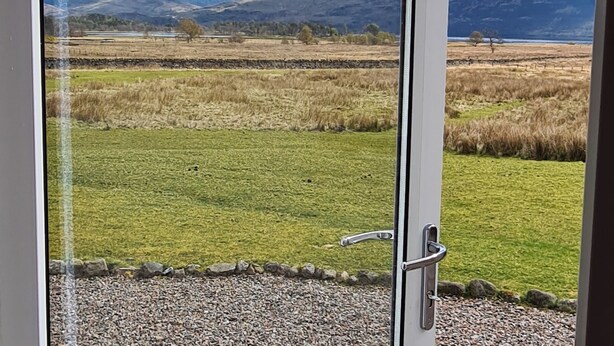 A view through a glass door of a grassy field with mountains in the background. - 3 bedroom accommodation in Ardgour, near Fort William (Ardgour, near Fort William)