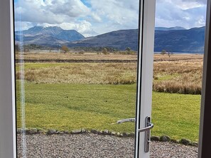 A view through a glass door of a grassy field with mountains in the background.