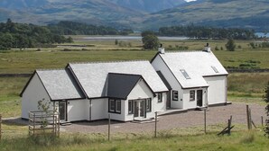 A white building with a sloped roof, a fenced yard, and a mountainous backdrop. - 3 bedroom accommodation in Ardgour, near Fort William (Ardgour, near Fort William)