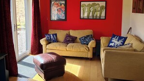 A living room with a beige sofa, a brown ottoman, and a red accent wall. - 3 bedroom accommodation in Ardgour, near Fort William (Ardgour, near Fort William)