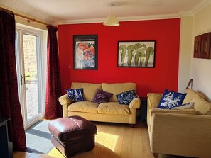 Uma sala de estar com sofá bege, um banquinho marrom e uma parede em tom de vermelho.