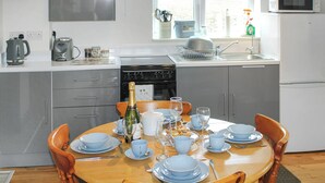 A modern kitchen with grey cabinets, a dining table set with blue dishes, and a bottle of champagne. - 1 bedroom accommodation in Stalham (Stalham)