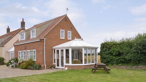 A brick house with a conservatory, a lawn, and a picnic table. - 1 bedroom accommodation in Stalham (Stalham)