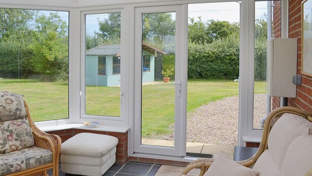 A conservatory with a white chair, a white sofa, and a patterned rug. - 1 bedroom accommodation in Stalham (Stalham)