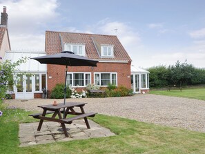 A brick house with a conservatory, a patio table with an umbrella, and a gravel driveway.