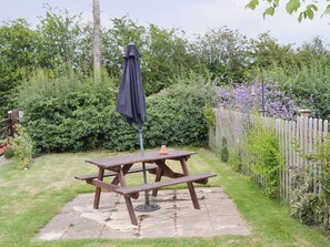 A picnic table with a black umbrella, surrounded by lush greenery and a wooden fence.