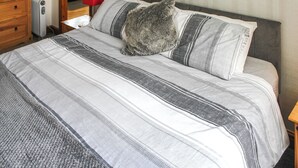 A neatly made bed with striped bedding, a wooden dresser, a red lamp, and a framed picture on the wall. - 1 bedroom accommodation in Stalham (Stalham)
