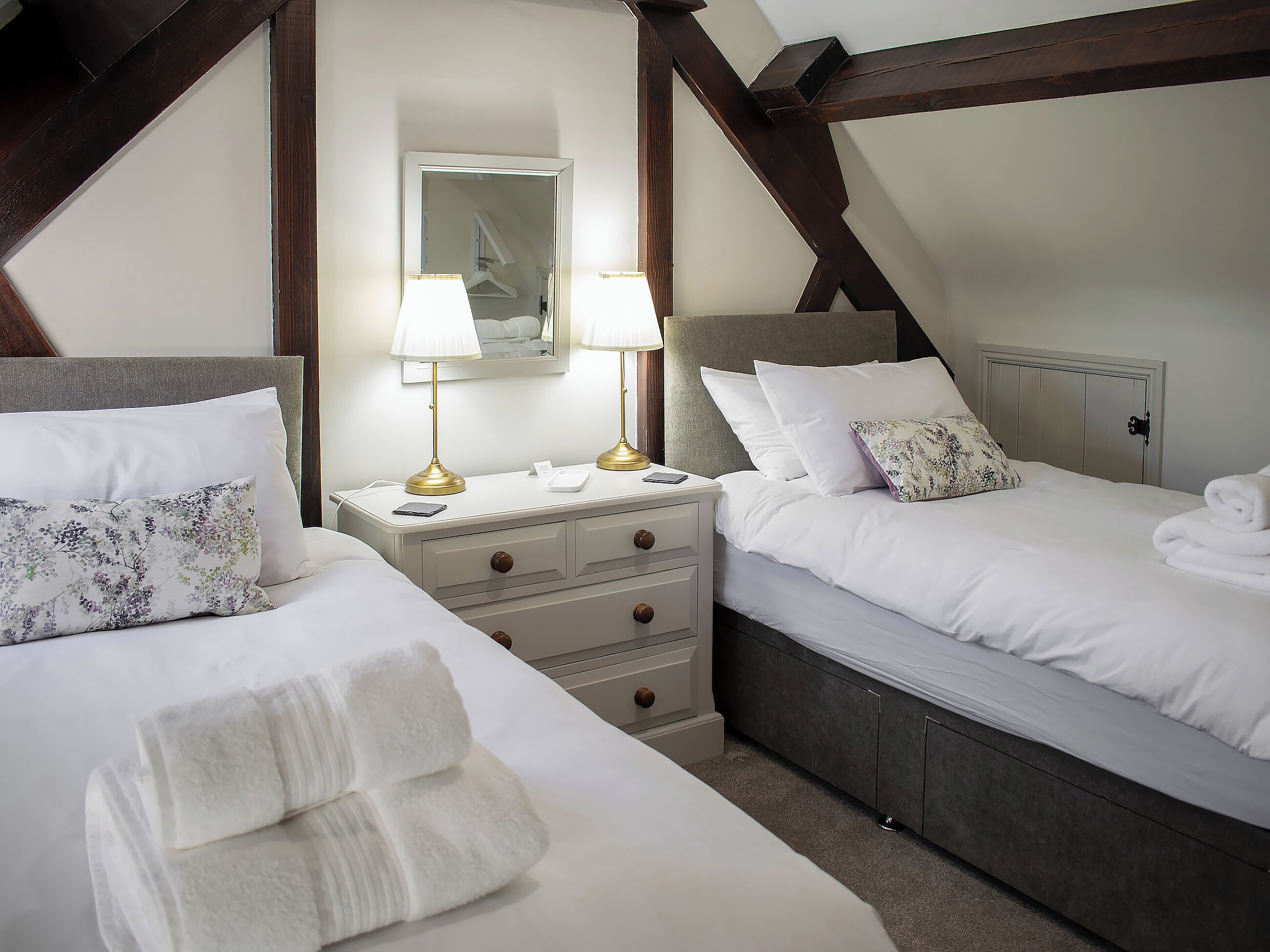 A hotel room with two beds, a bedside table with lamps, a mirror, and a wardrobe.