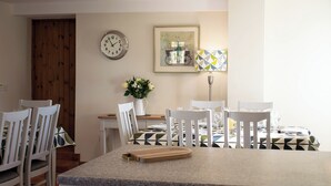 A dining area with a kitchen island, white chairs, a clock, a framed picture, and a vase with flowers. - Characterful, rural barn conversion. (Heathcote, near Hartington)
