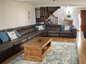 A living room with a brown leather sectional sofa, a wooden coffee table, a patterned rug, and a staircase in the background.