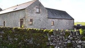 A stone building with a sloped roof, a small window, and a weather vane. - Characterful, rural barn conversion. (Heathcote, near Hartington)