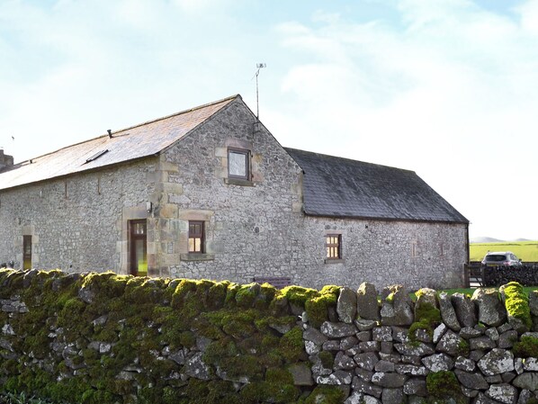A stone building with a sloped roof, a small window, and a weather vane.