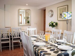 A dining area with a table set for four, chairs, a mirror, a clock, and a vase with flowers.