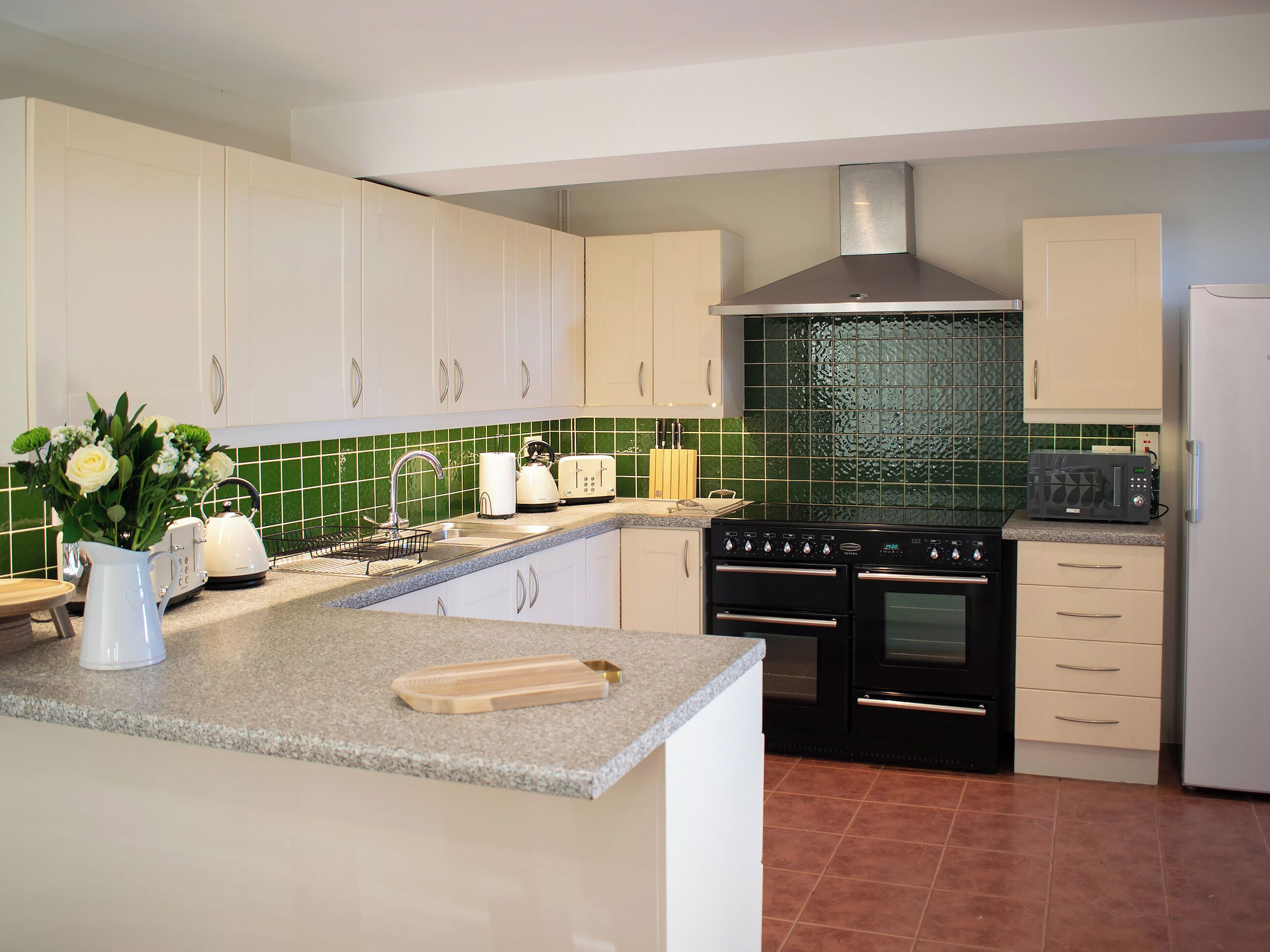 Una cocina con armarios blancos, salpicadero de azulejos verdes, estufa, horno y microondas.