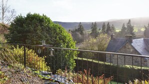 Ein Steinhäuschen mit traditioneller Gestaltung, umgeben von üppiger Vegetation und Blick auf sanfte Hügel.