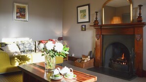 Ein gemütliches Wohnzimmer mit Kamin, einer Couch, einem Couchtisch mit Teeservice und einem Blumenstrauß.