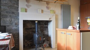Eine Küche mit Steinwand, Kaminofen, Holzschrank und Tisch mit kariertem Tischläufer.