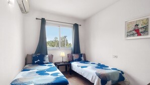 Una camera da letto con due letti singoli, un comodino con una lampada, una finestra con tende e un quadro appeso al muro.