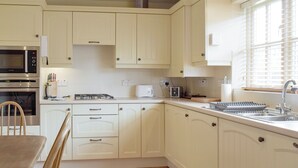 Una cocina con armarios blancos, estufa, microondas y pileta.