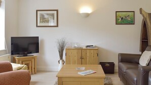 Una sala de estar con una televisión de pantalla plana, un mueble de madera, una mesa de centro, un sofá y dos cuadros en la pared.