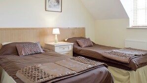 Un dormitorio con dos camas, una mesita de noche, una lámpara, un cuadro en la pared y una ventana con persianas.