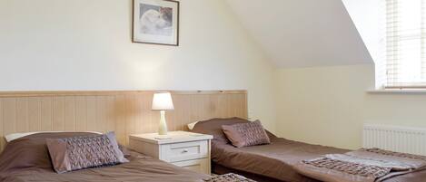 A bedroom with two beds, a nightstand, a lamp, a framed picture on the wall, and a window with blinds.