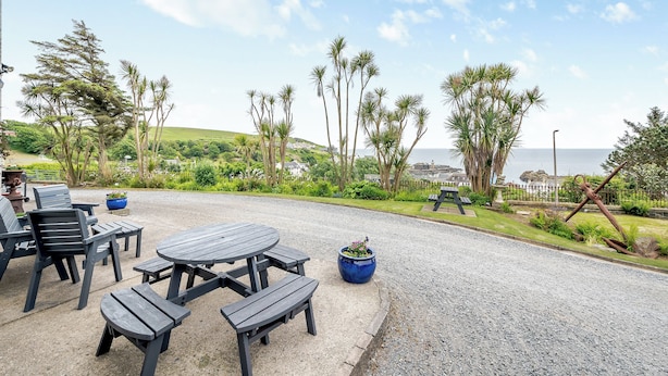 An outdoor seating area with a table and benches, surrounded by palm trees and a view of the ocean. - 7 bedroom accommodation in Portpatrick (Portpatrick)