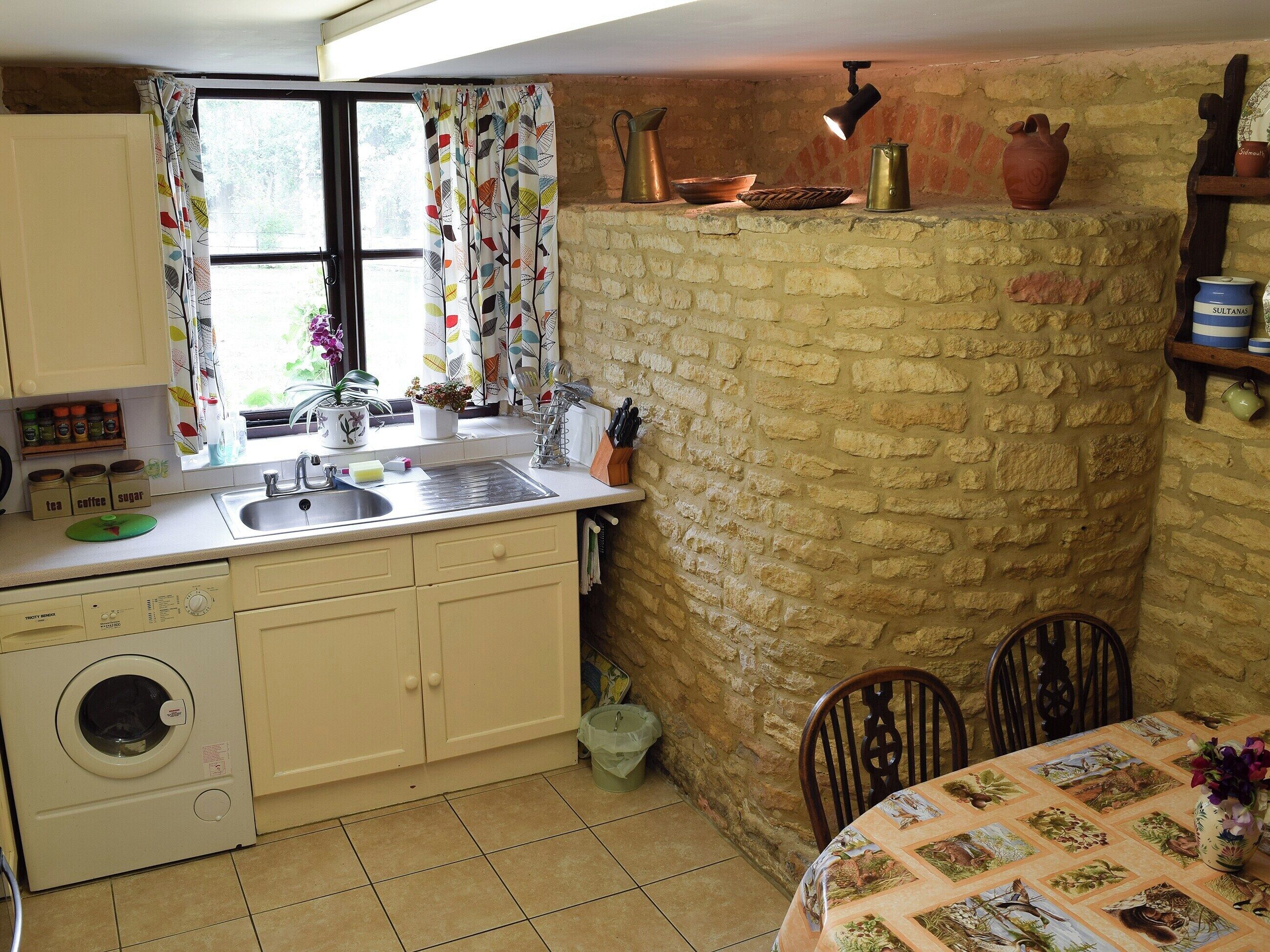 A kitchen with a washing machine, sink, and a table with a quilted tablecloth.