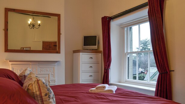Un dormitorio con cama, cómoda, televisor, ventana con cortinas y espejo.