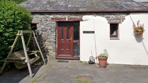 A rustic cottage with a stone wall, a wooden door, and a small window. - A pretty 2 bedroom barn conversion set within an equestrian centre. (Polson, nr. Launceston)