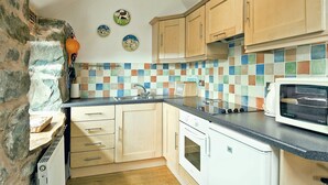 Cozinha com armários de madeira, painel de azulejos e micro-ondas.