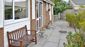 A wooden bench outside a house with a brick facade and white shutters. - 3 bedroom accommodation in Fairbourne (Fairbourne)