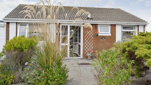 A two-story house with a tiled roof, a front door, and a small garden area with various plants and shrubs. - 3 bedroom accommodation in Fairbourne (Fairbourne)