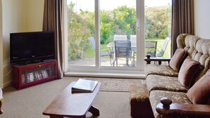 A living room with a television, a sofa, a coffee table, and a sliding glass door leading to a patio with outdoor furniture. - 3 bedroom accommodation in Fairbourne (Fairbourne)