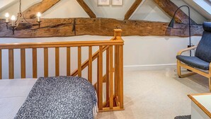 A cozy attic bedroom with exposed wooden beams, a wooden railing, a bed, a chair, and framed pictures on the wall. - 2 bedroom accommodation in Almondbury (Almondbury)