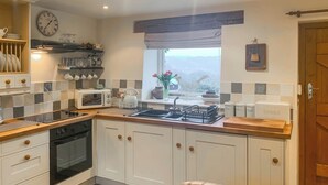 A modern kitchen with white cabinets, a built-in oven, a microwave, and a stove. There is a window with a view of the outdoors, and a clock on the wall. - 2 bedroom accommodation in Almondbury (Almondbury)