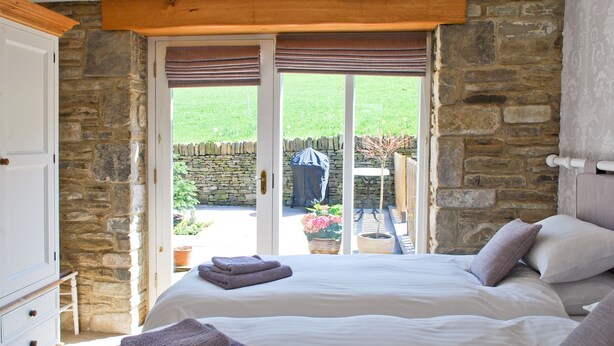 A bedroom with two beds, stone walls, and a view of a garden. - 2 bedroom accommodation in Almondbury (Almondbury)