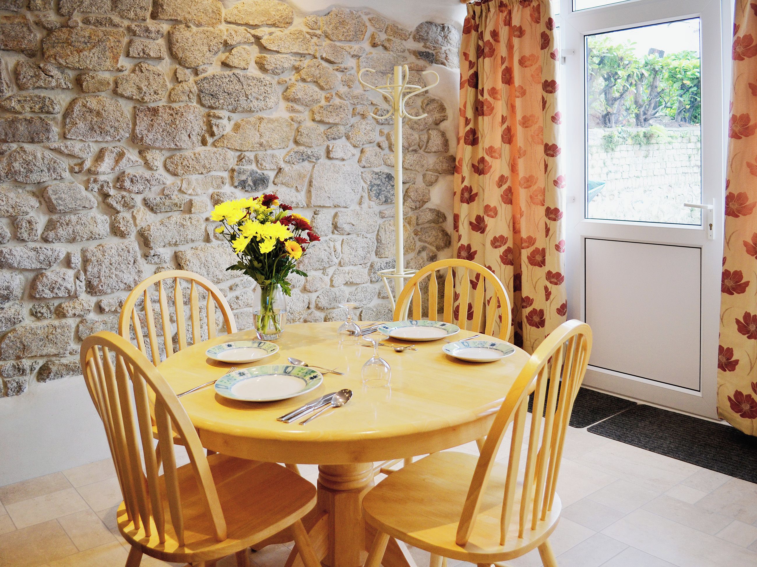 A dining area with a stone wall, a table set for four, and a window with curtains.