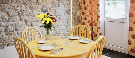 A dining area with a stone wall, a table set for four, and a window with curtains.